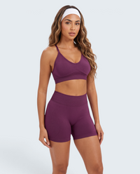 Modelo veste conjunto desportivo roxo escuro VD Beyond Limits com top e calções seamless de cintura subida.