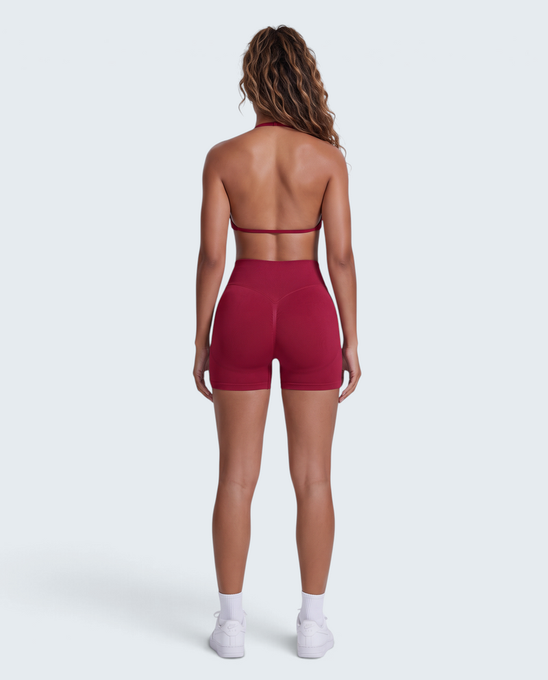 Vista traseira de modelo com conjunto desportivo VD Beyond Limits bordeaux, top halter e calções seamless modeladores.