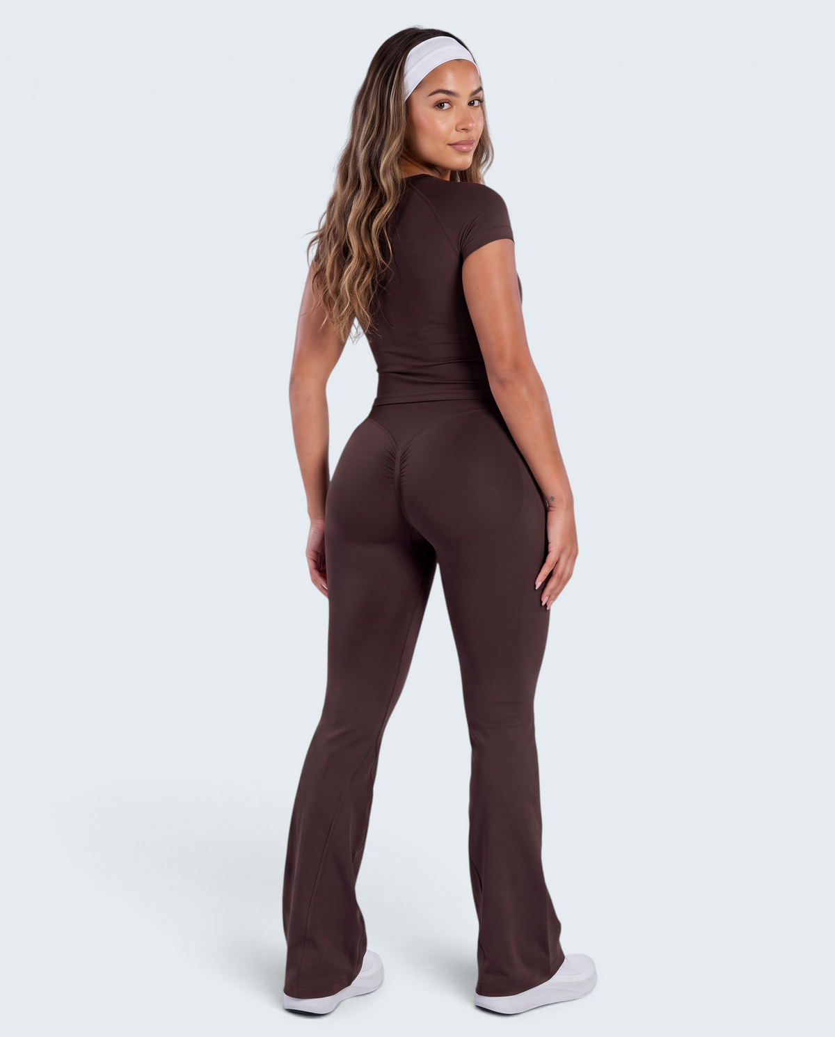 Modelo veste conjunto castanho VD Beyond Limits com t-shirt justa e calças flare de cintura alta para desporto.
