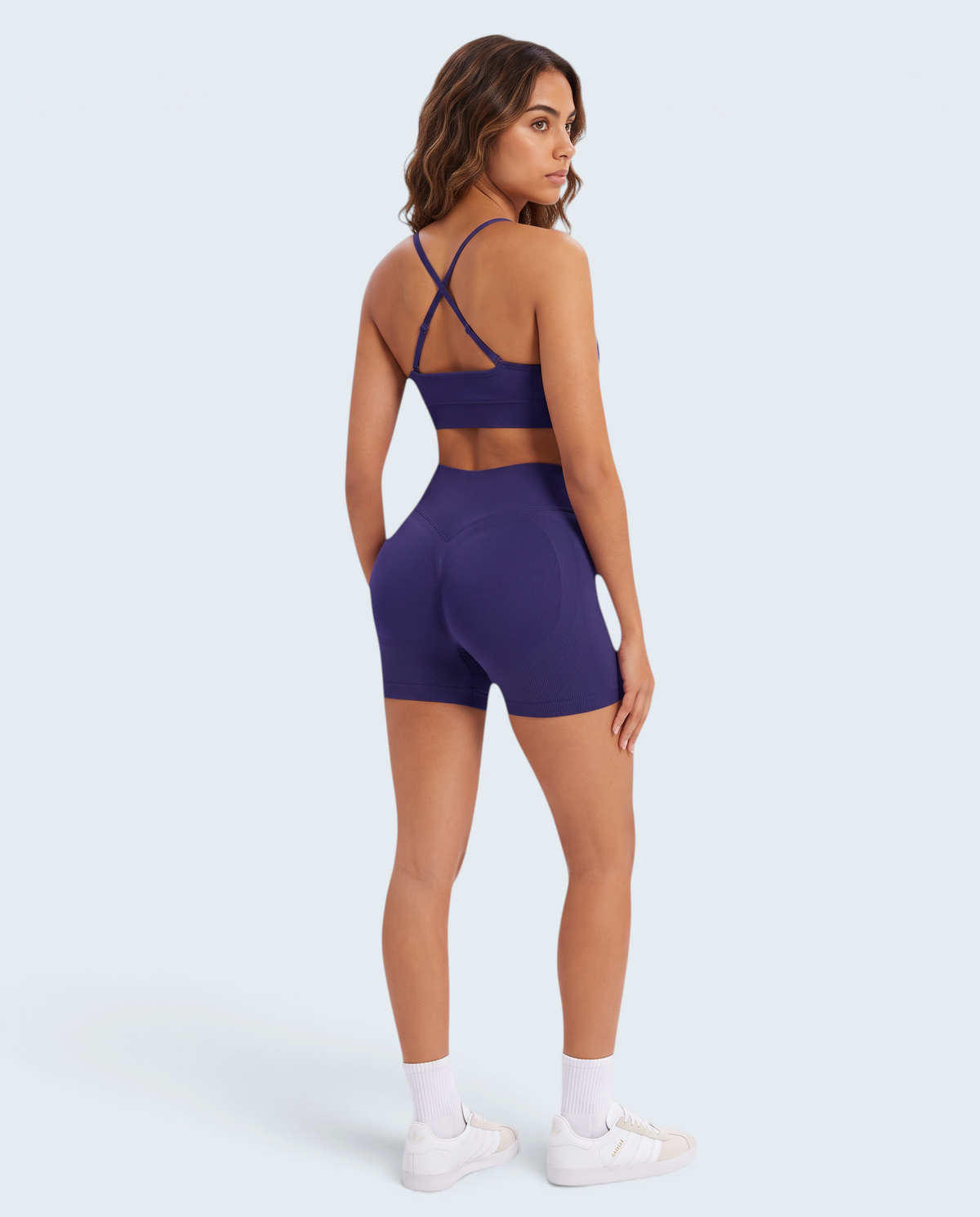 Modelo veste conjunto desportivo roxo escuro VD Beyond Limits com top de alças cruzadas e calções seamless