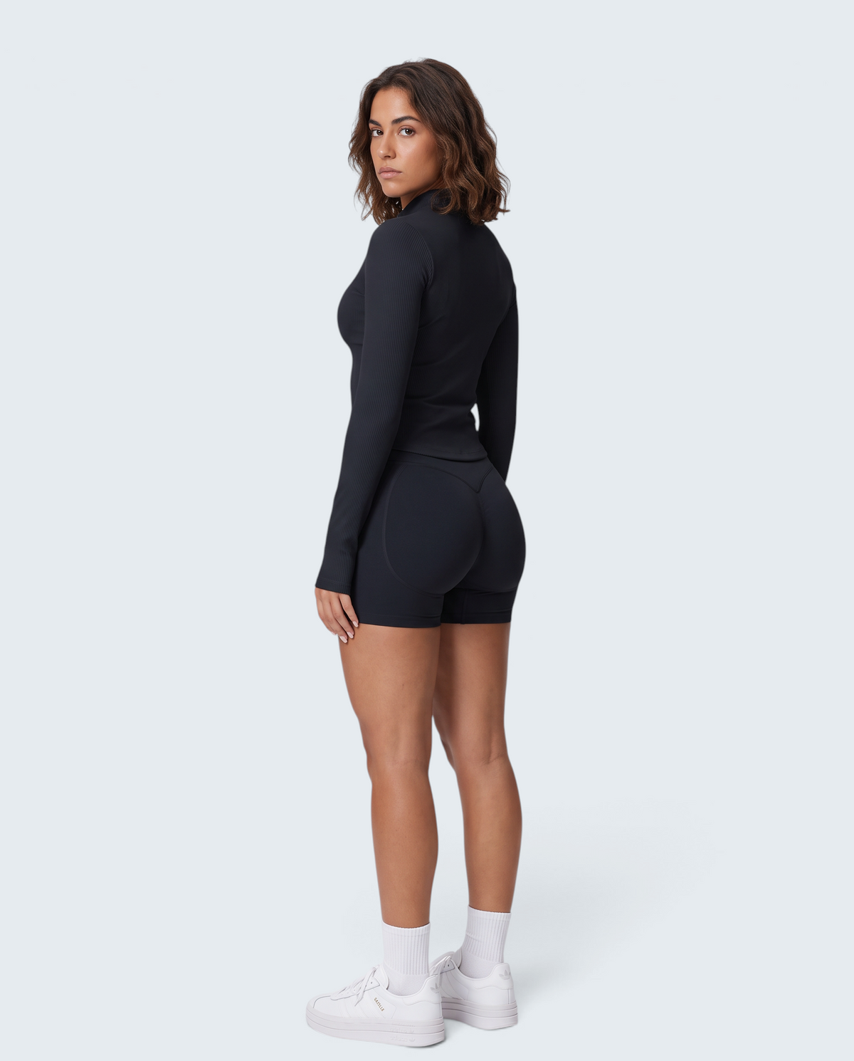 Modelo veste conjunto desportivo preto VD Beyond Limits com casaco de fecho e calções seamless de cintura subida.
