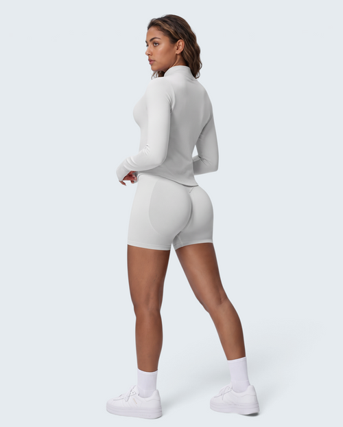 Modelo veste conjunto VD Beyond Limits branco seamless com casaco de fecho e calções de cintura subida para treino.