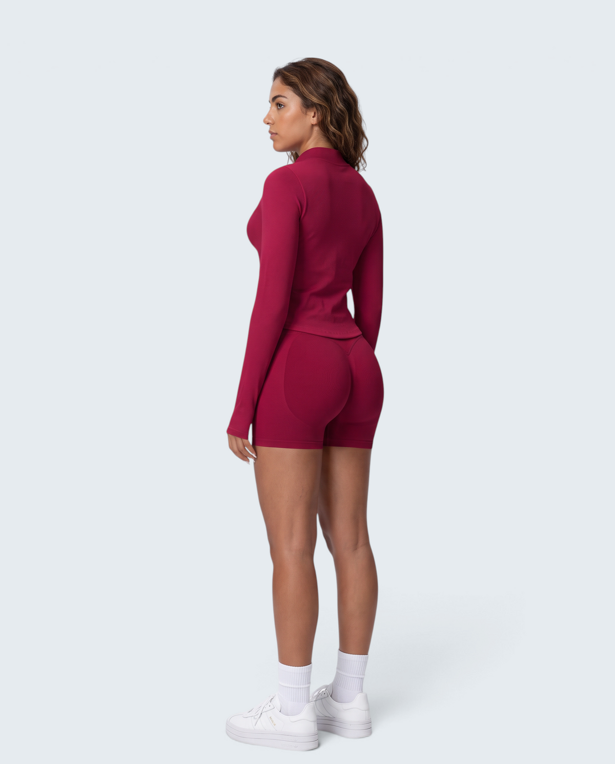 Modelo de perfil vestindo conjunto seamless vermelho VD Beyond Limits com casaco de fecho e calções de cintura subida.