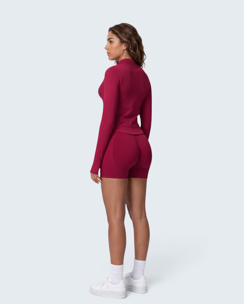 Modelo de perfil vestindo conjunto seamless vermelho VD Beyond Limits com casaco de fecho e calções de cintura subida.