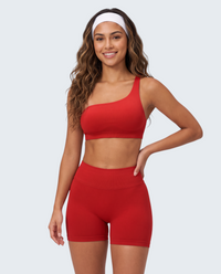 Modelo sorridente veste conjunto seamless vermelho VD Beyond Limits com top assimétrico e calções de cintura subida.