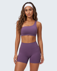 Modelo veste conjunto seamless roxo VD Beyond Limits com top de um ombro e calções de cintura subida para treino.