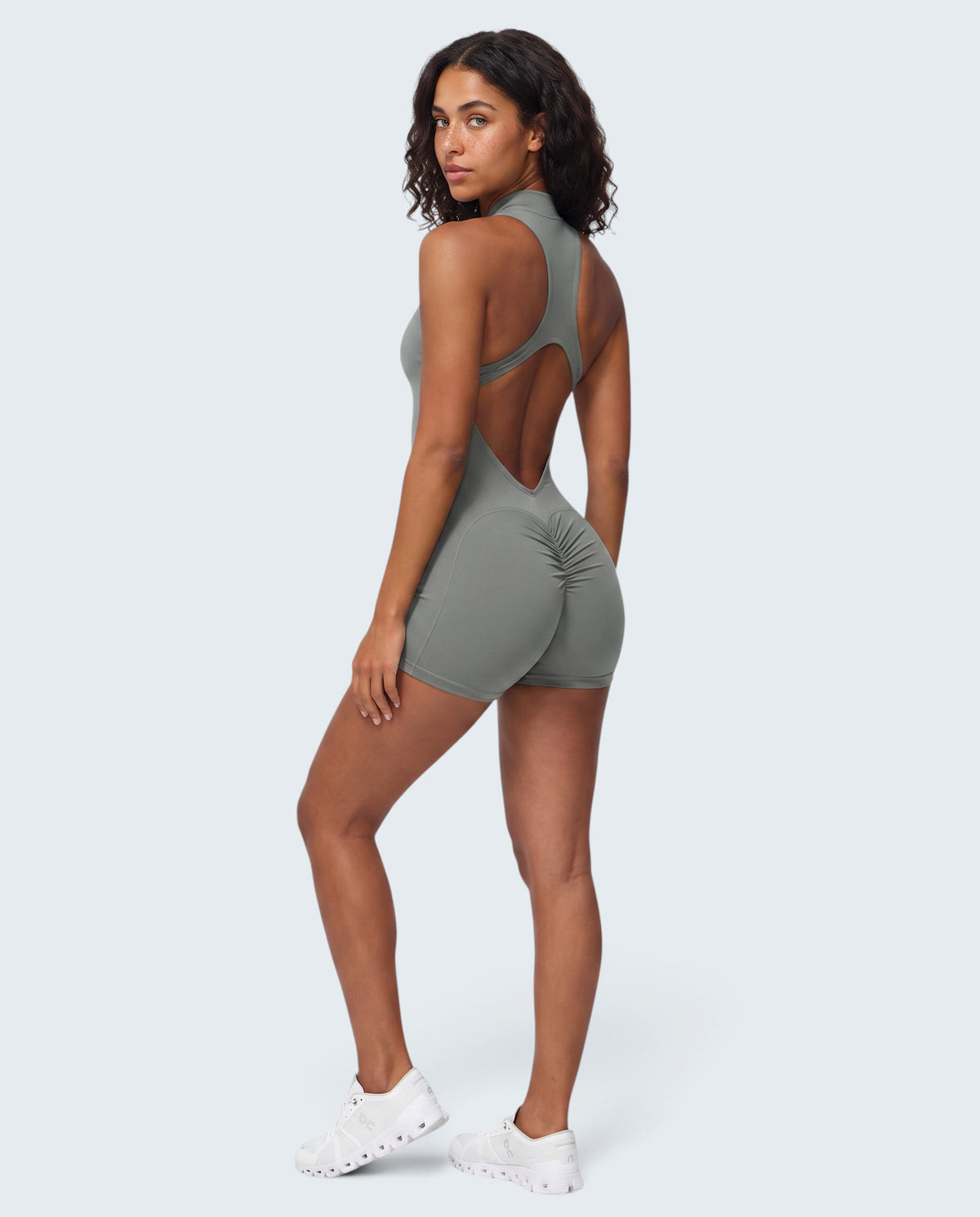 Modelo veste macacão curto seamless cinzento VD Beyond Limits com costas abertas e detalhe franzido para treino